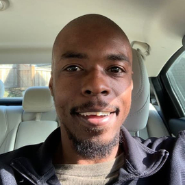 A close up photo of Logan Willoughby sitting in the interior of a car wearing a dark blue jacket.