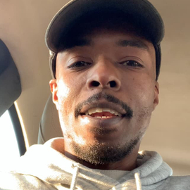 A self shot image of Logan Willoughby from below, wearing a light hooded sweatshirt and baseball cap.