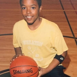 Logan Willoughby as a boy holding a basketball and wearing a bright, yellow shirt.