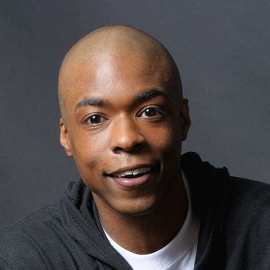 A professional image of Logan Willoughby wearing a white t shirt and dark hooded sweatshirt.